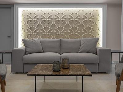 Modernes Wohnzimmer mit grauem Sofa, gemusterter beleuchteter Wand und Tisch mit Dekoration.