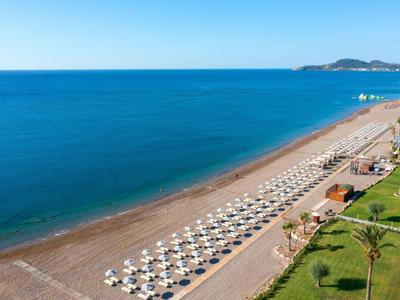 Strand mit vielen Sonnenschirmen und Liegestühlen entlang einer Küste bei klarem Himmel.
