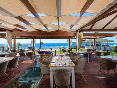 Area ristorante aperta con vista sul mare e sulla spiaggia, tavoli apparecchiati e sedie comode.