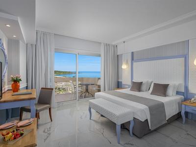 Modernes Hotelzimmer mit Doppelbett, Balkon und Blick auf den Pool und die Stadt.