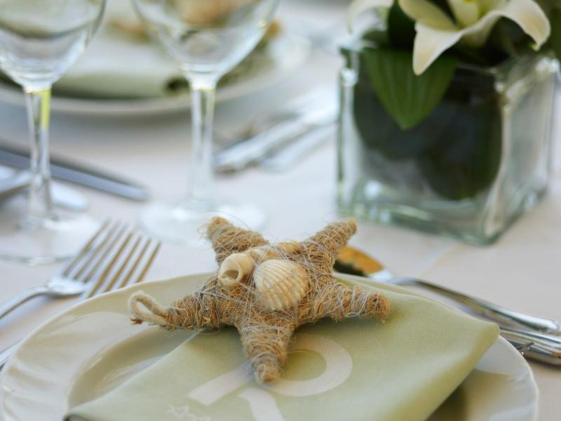 Gedeckter Tisch mit Sternmuschel auf grünem Serviette und Blumenarrangement.