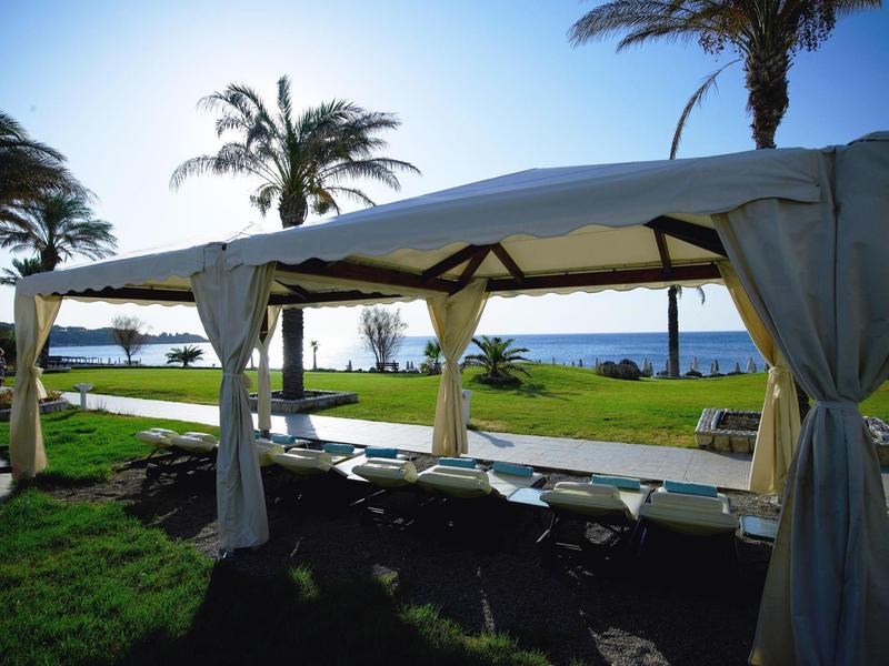 Pavillon mit Liegestühlen auf Grasfläche mit Blick aufs Meer bei klarem Himmel.