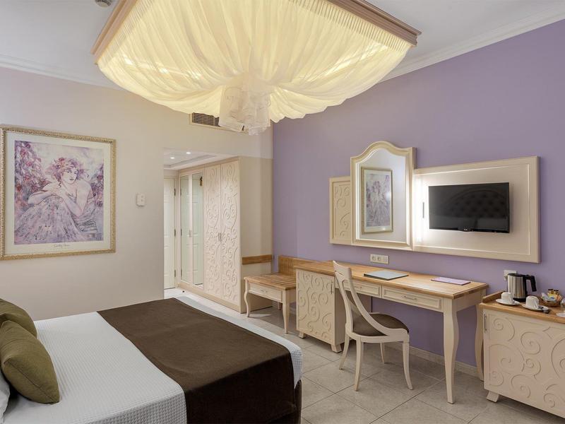 Gemütliches Hotelzimmer mit Doppelbett, Schreibtisch, Fernseher und lila Wandfarben.