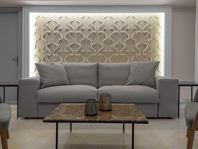 Modernes Wohnzimmer mit grauem Sofa, gemusterter beleuchteter Wand und Tisch mit Dekoration.