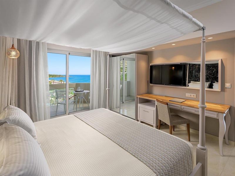 Helles Hotelzimmer mit Blick auf das Meer, Balkon, Doppelbett und modernem Schreibtisch.
