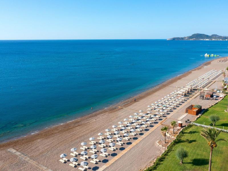 Strand mit vielen Sonnenschirmen und Liegestühlen entlang einer Küste bei klarem Himmel.