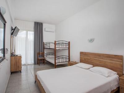 Schlicht eingerichtetes Hotelzimmer mit Doppelbett und Etagenbett, heller Wandfarbe, Fernseher und Balkon.