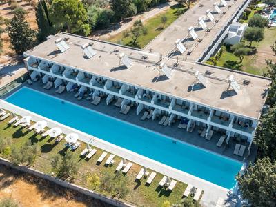 Moderner Hotelkomplex mit großem Außenpool und Liegestühlen in einer grünen Umgebung.