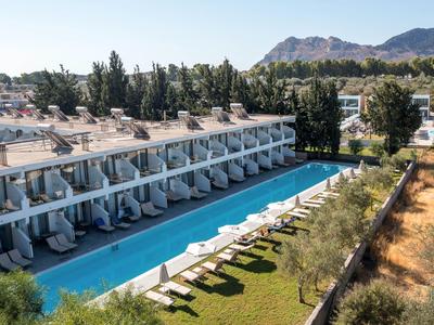 Moderner Hotelkomplex mit Pool und Liegestühlen, umgeben von Bäumen und Bergen im Hintergrund.