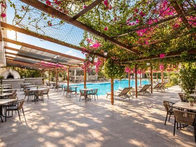 Hotelterrasse mit Tischen, Stühlen, blühenden Pflanzen und einem Pool im Hintergrund.