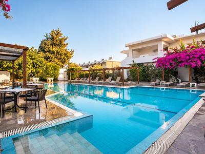 Moderner Swimmingpool neben Hotelgebäude mit Sitzgelegenheiten und blühenden Pflanzen.