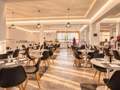 Helles, modernes Restaurant mit vielen Tischen und Sesseln in Schwarz und Hellholz.