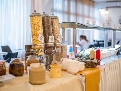 Buffet mit verschiedenen Müslisorten, Joghurt und Toppings in einem hellen Speisesaal.