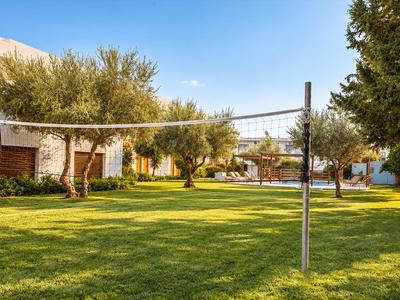 Großer grüner Garten mit Bäumen und Volleyballnetz bei klarem Himmel, ideal für Urlaub.