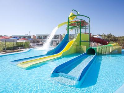 Wasserpark mit bunten Rutschen und Planschbecken unter blauem Himmel in einem Urlaubsressort.