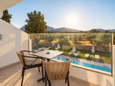 Balkon mit Tisch und Stühlen bietet Blick auf Pool, Garten und Berge im Sonnenlicht.