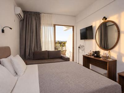 Modernes, helles Hotelzimmer mit Doppelbett, Sofa, großem Spiegel und Zugang zu einem Balkon.