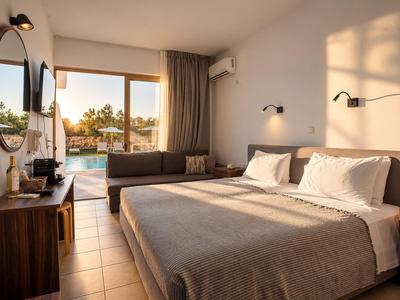 Helles Hotelzimmer mit Doppelbett, Sofa, Holzmöbeln und Blick auf Pool und Palmen.