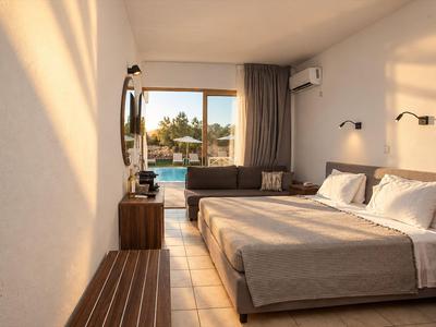 Modernes Hotelzimmer mit Doppelbett, Sofa und Blick auf den Pool durch eine Glasschiebetür.