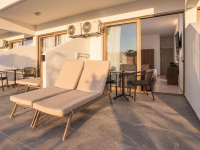 Moderner Balkon mit Liegestuhl und Tisch vor offenem Hotelzimmer bei Sonnenuntergang.