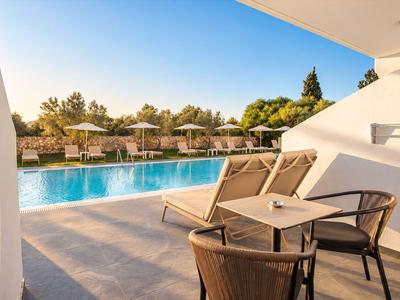 Moderner Hotelpool mit Sonnenliegen und Tischen bei klarem Himmel am Nachmittag.