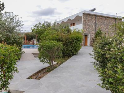 Moderner Steinhaus mit Pool, umgeben von Büschen und Bäumen auf einem gepflasterten Weg.