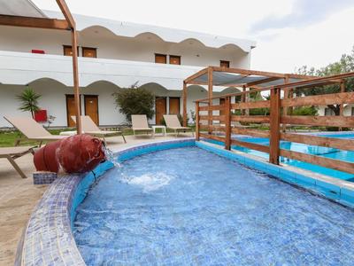 Kleiner Pool mit Wasserspiel und Holzgeländer vor einem weißen Hotel mit Zimmern und grünen Pflanzen.