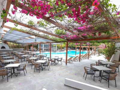 Hotelterrasse mit Tischen, Stühlen und blühendem Weinlaub über dem Sitzbereich neben dem Pool