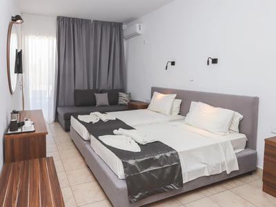 Modern hotelkamer met tweepersoonsbed, bank, bureau en lichte tegelvloer.