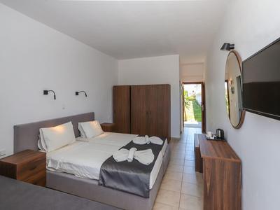 Licht ingericht hotelkamer met tweepersoonsbed, kast, spiegel en tv aan de muur.