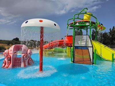 Kleurrijke glijbaan en speeltoestellen in een zwembad van een waterpark onder een bewolkte hemel.