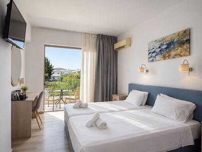 Helles Hotelzimmer mit zwei Betten, Balkon und Blick auf die Natur.