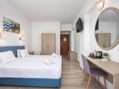 Modernes Hotelzimmer mit zwei Betten, Schreibtisch, Fernseher und Kleiderschrank.