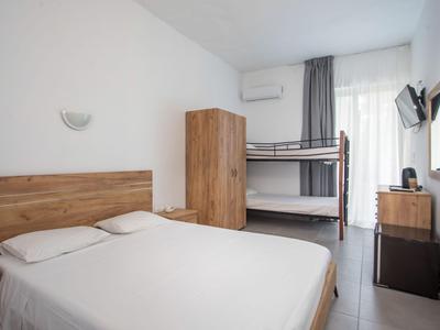 Ein modernes Hotelzimmer mit Doppelbett, Etagenbett, Schrank und Fenster mit Vorhängen.