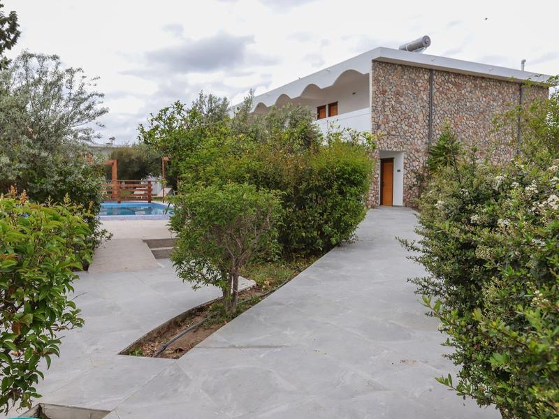 Modern stenen gebouw met zwembad en groene struiken eromheen onder bewolkte hemel.