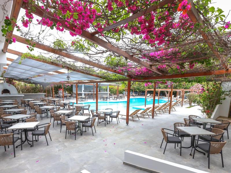 Hotelterras met tafels, stoelen en bloeiende wijnstokken boven zitgedeelte bij het zwembad