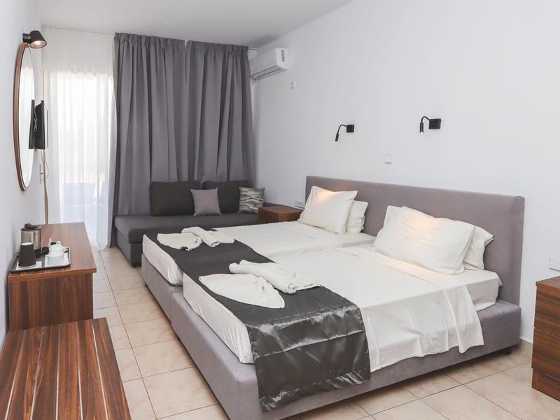 Modern hotelkamer met tweepersoonsbed, bank, bureau en lichte tegelvloer.