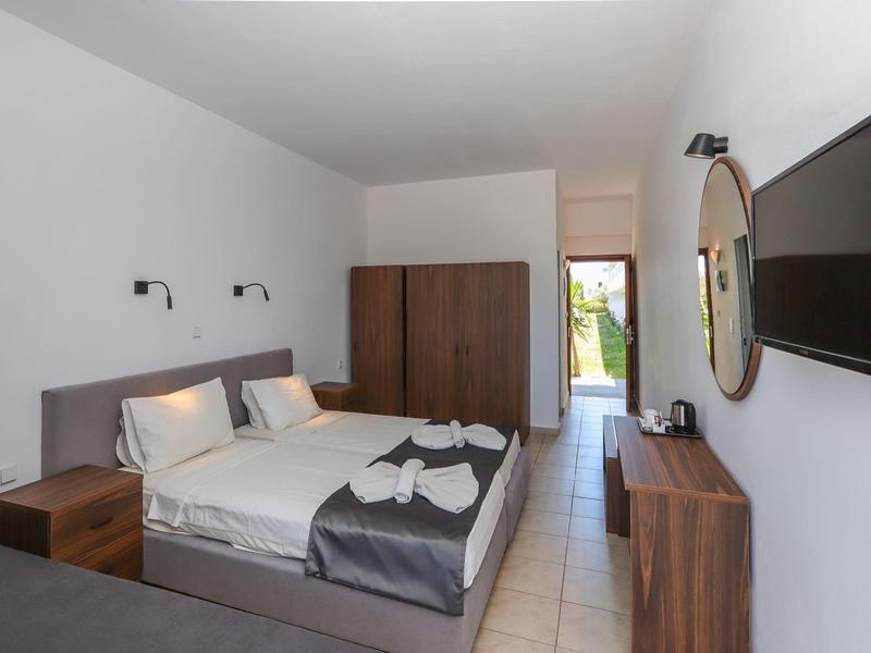 Licht ingericht hotelkamer met tweepersoonsbed, kast, spiegel en tv aan de muur.