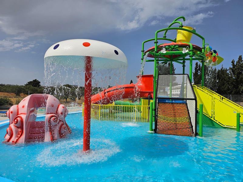 Kleurrijke glijbaan en speeltoestellen in een zwembad van een waterpark onder een bewolkte hemel.