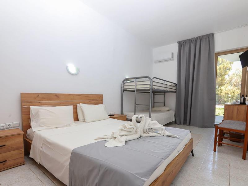 Hotelkamer met tweepersoonsbed, stapelbed, bureau en raam met uitzicht naar buiten.