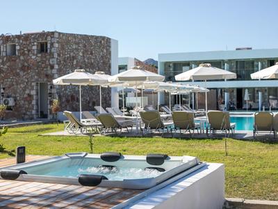 Hotelanlage mit Pool, Liegestühlen und Sonnenschirmen auf einer Rasenfläche bei klarem Himmel.