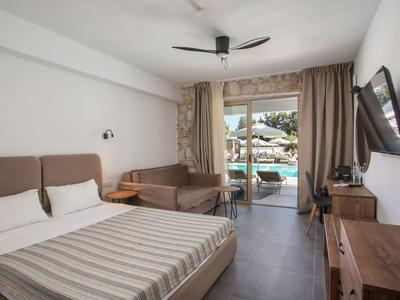 Modernes Hotelzimmer mit Doppelbett, Fernseher, Schreibtisch und Zugang zum Poolbereich.