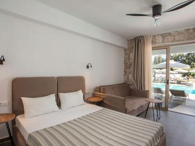Hell eingerichtetes Hotelzimmer mit Doppelbett, Sofa und Blick auf den Pool durch die Terrassentür.