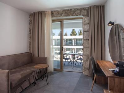 Moderner Hotelzimmerbereich mit Sofa, Tisch, Schreibtisch und Balkon mit Blick auf benachbarte Gebäude.
