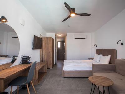 Modern eingerichtetes Hotelzimmer mit Bett, Sofa, Schreibtisch und Deckenventilator.