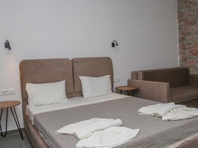 Modernes Hotelzimmer mit Doppelbett, zwei Nachttischen und braunem Sofa vor grauer Wand.