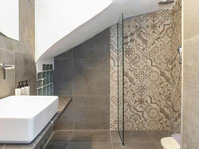 Modernes Badezimmer mit weißem Waschbecken, Glastür und verzierten Wandfliesen.