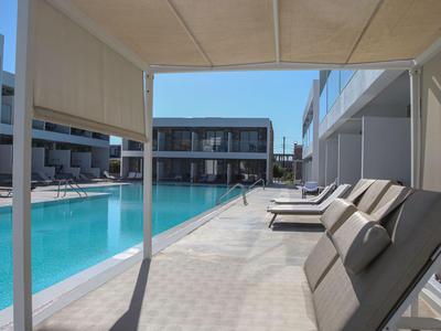Moderner Hotelpool mit Liegestühlen und Sonnenschirmen unter klarem Himmel.