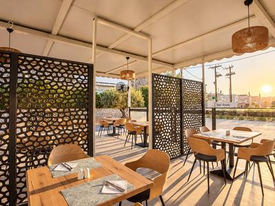 Offener Hotel-Outdoor-Bereich mit Holztischen, bequemen Stühlen und dekorativen Trennwänden bei Sonnenuntergang.