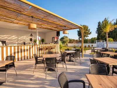 Outdoor-Cafébereich mit Holztischen und schwarzen Stühlen unter Sonnendach bei klarem Himmel.